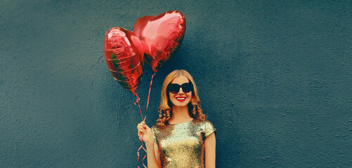 Portrait of happy smiling young woman with red heart shaped balloons on dark background