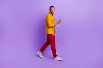 Fototapeta na wymiar Full size profile photo of positive person walking hold use telephone isolated on violet color background