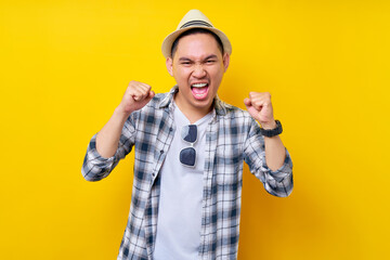 Fototapeta na wymiar excited fun Young handsome ethnic Asian man 20s wearing casual clothes hat making winner gesture celebrating clenching fists saying yes isolated on yellow background. People lifestyle concept