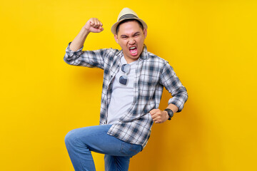 excited fun Young handsome ethnic Asian man 20s wearing casual clothes hat making winner gesture celebrating clenching fists saying yes isolated on yellow background. People lifestyle concept