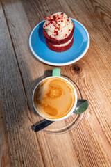 Fototapeta na wymiar Imagen gastronómica de un café con leche en una taza verde y un pastel de red velvet en un plato azul sobre una mesa de madera.