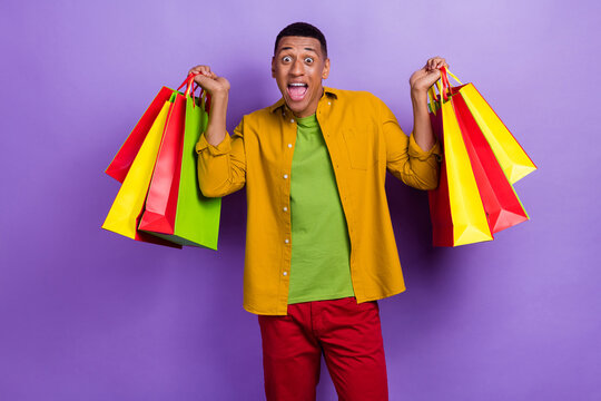 Photo of ecstatic impressed optimistic guy dressed yellow shirt holding shopping bags new clothes isolated on violet color background