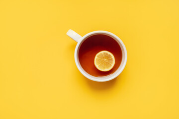 
black lemon tea in a large cup on a yellow background with a yellow blanket and lemons. copy...