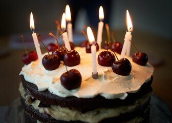 A close up of cherries on a Black Forest Gateau birthday cake with lit candles on it.