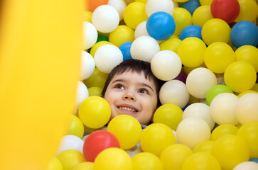 Fototapeta na wymiar kid having fun in play center pool with colorful many balls.happy smiling child preschooler boy throwing tossing up plastic balls playground interior inside mall.soft ocean plastic balls cover face