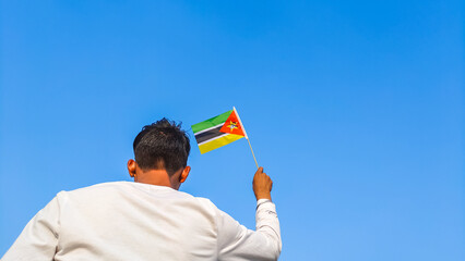 Boy holding Mozambique flag against clear blue sky. Man hand waving Mozambican flag view from back, copy space