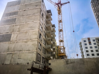 Tower crane at the construction site against the background of the summer sky. Concrete panel high-rise buildings under construction