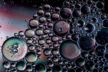 Oil bubbles on the surface of water refracting colours underneath as backdrop or wallpaper giving a moody effect.
