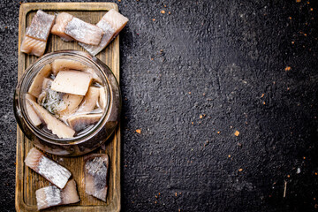 Salted herring in a glass jar on a cutting board. 