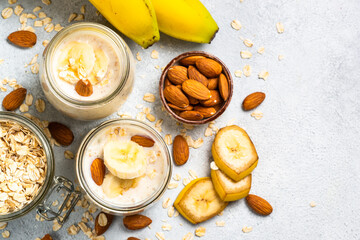 Almond banana smoothie with oat flakes in glass jars at white stone table. Top view.