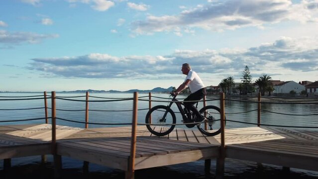 Man over 60 years old riding an electric bicycle on a footbridge over the sea on a nice sunny day. concept enjoy life. second youth
