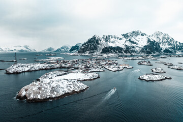 Drone aerial shots, photos in Henningsvaer, Lofoten Norway during cloudy weather winter time with snowy epic mountains, lot of islands and amazing light. Old fishing village with boats and ships. 