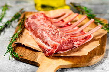 Raw rack of lamb on a cutting board with oil and rosemary. 