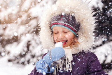Child Have fun in Snowy Winter park. Baby Girl Eat cold Snow, Enjoying Life. Children in Winter