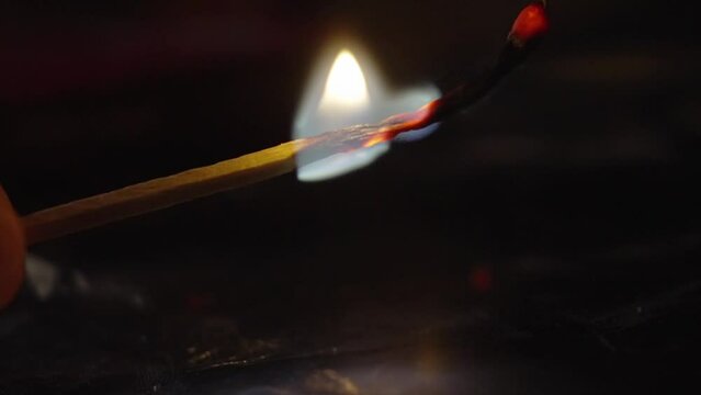 Match lighting up and burning flame against black background.
