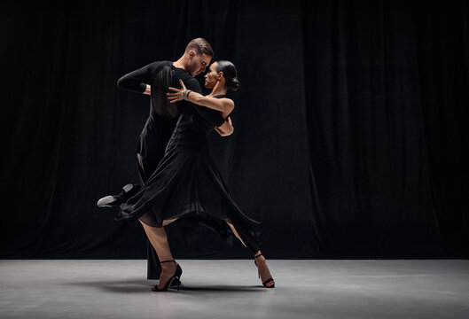 Man and woman, professional tango dancers performing in black stage costumes over black background. Expression of togetherness. Concept of hobby, lifestyle, action, motion, art, dance aesthetics