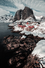 Iconic view on red cabins in Hamnoy in Norway Lofoten during winter with snow and mountains in background