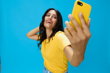 Woman with a phone in her hands with a yellow case on a blue background in a yellow T-shirt, emotions signals gestures, online lifestyle concept, shopping, communication, learning, business online