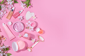 Spring skin care cosmetics flat lay. Beauty facial care cosmetics: serum, cream, mask on pink sunny background with spring blossom flowers, top view copy space