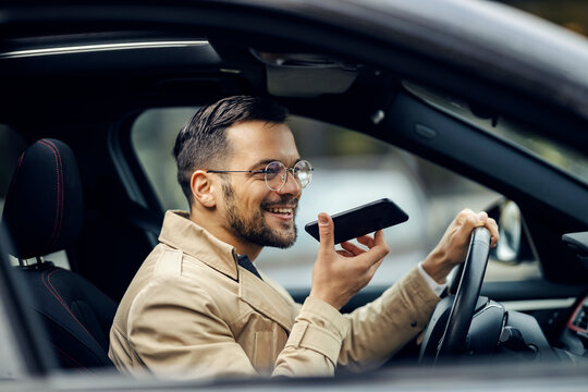 A happy businessman is driving his car and leaving voice massage on the phone.