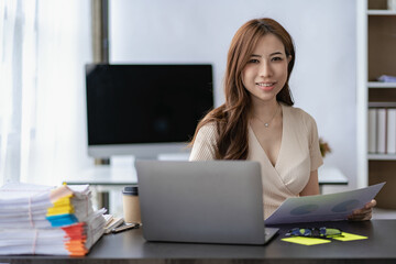 Asian businesswoman working with financial documents and laptop Inside office worker calculating financial indicators smiling and happy with success and results of business success