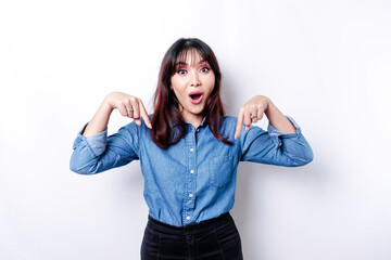 Shocked Asian woman wearing blue shirt pointing at the copy space below her, isolated by white background