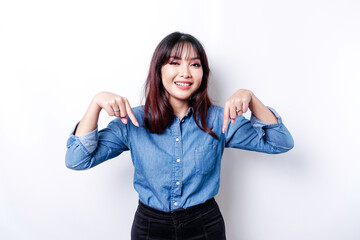 Excited Asian woman wearing blue shirt pointing down at the copy space, isolated by white background