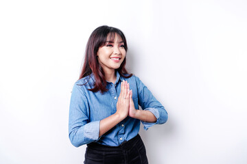 Smiling young Asian woman wearing blue shirt, gesturing traditional greeting isolated over white background