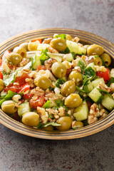Vegetarian green olives salad with walnuts, tomatoes, cucumbers seasoned with pomegranate molasses close-up in a plate on the table. Vertical