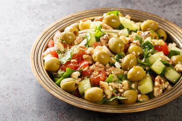 Turkish green olives salad with walnuts, tomatoes, cucumbers, parsley close-up in a plate on the table. Horizontal