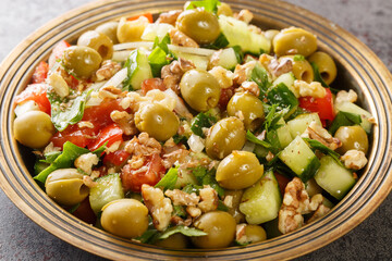 Healthy vegetarian vegetable salad with green olives, walnuts, tomatoes, cucumbers, parsley close-up in a plate on the table. Horizontal