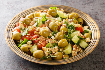 Homemade green olives salad with walnuts, tomatoes, cucumbers, parsley close-up in a plate on the table. Horizontal