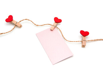 Wooden decorative clothespins with red hearts and a blank greeting card on a rope isolated on a white background. Valentine's Day concept. Love. Copy space.	