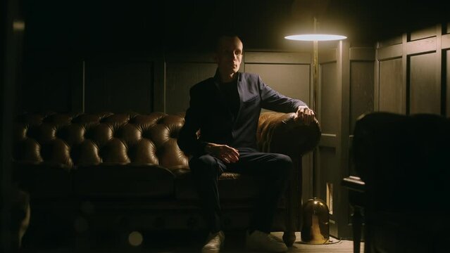 enigmatic man moving like robot sitting alone in dark living room, strange madman