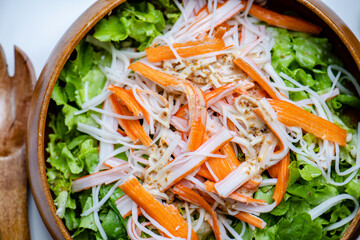 Hand mix fresh baby cos salad and crab stick in wood blow. Organic Vegetables mix lunch with green salad at kitchen table in wood cutting board.