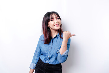 Excited Asian woman wearing blue shirt pointing at the copy space beside her, isolated by white background