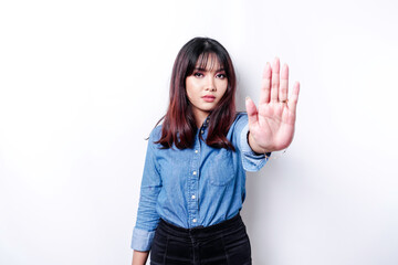 Beautiful Asian woman wearing blue shirt with hand gesture pose of stop or prohibition with copy...