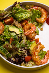 bulgur salad with shrimp greens cheese cherry tomatoes on a white plate on a yellow background