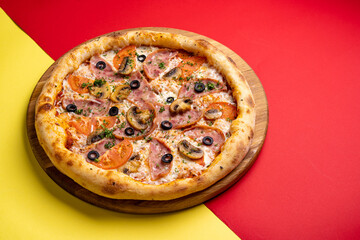 pizza with ham, tomatoes, mushrooms and olives on a board on a colored red-yellow background