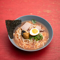 Ramen noodles with meat and egg in broth. Plate of ramen on table. Nori leaf decoration. Serving dish. Red background, top view. 