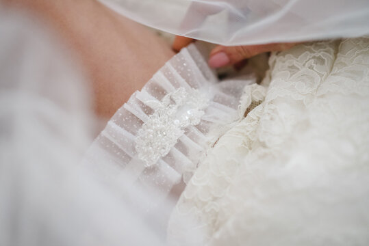 Bride dresses garter on the leg. Picture of beautiful female legs in wedding dress. Bride putting a wedding garter on her leg. Top view.