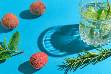 Creative composition made of glass with lemonade, green rosemary and lychee fruits on bright blue background with shadow. Summer refreshment concept.