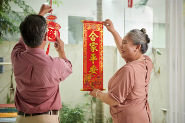 Senior couple decorating house with couplets with luck and prosperity wishes in new year