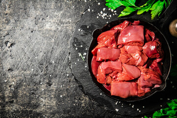 Pieces of raw liver in a frying pan with parsley and spices. 