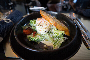 Caesar Salat mit Baguette und einem blanchiertem Ei auf schwarzem Steinteller