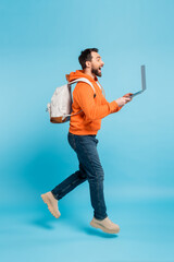 side view of excited student with backpack and laptop levitating on blue background.