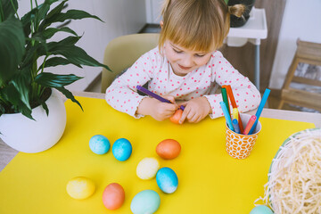 Smiling little girl with colorful eggs preparing for Easter Holiday. Kids painting easter eggs. Creative background for preschool and kindergarten. Family traditions and symbols of celebration.