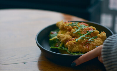 Fried chicken in breadcrumbs with tomato sauce and salad greens on black plate in cafe