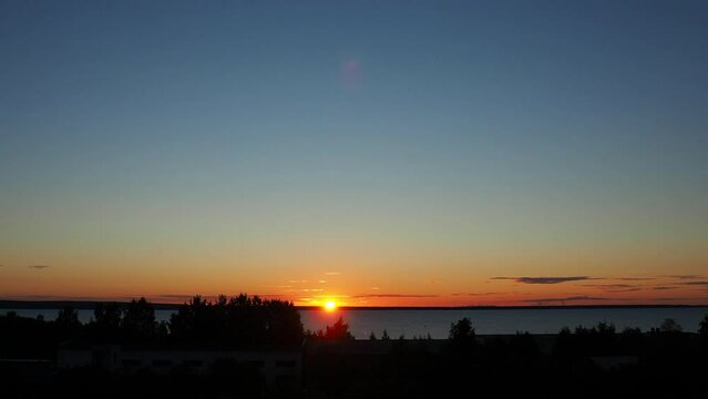 Yellow-orange dawn and sunrise in summer. Sunrise and the rise of the sun disk above the horizon. Rising sun. Clouds give way to clear blue skies. Time lapse 4k. Lifting sun disk. Glare of the sun