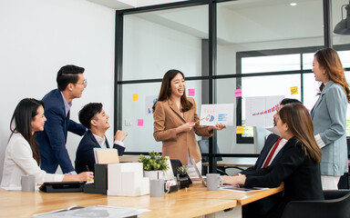 Smart confident business woman wearing formal suit, smiling with success, making presentation of marketing, design creative thinking plan in meeting room at indoor office with colleagues.